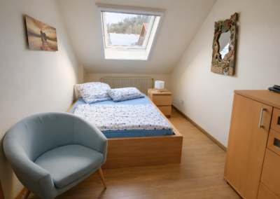 Gemütliches Schlafzimmer unter der Dachschräge mit Einzelbett, Dachfenster, Kommode und Sitzstuhl in der Ferienwohnung Jaeger in Viereth bei Bamberg.