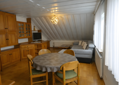 Wohn- und Essbereich der Ferienwohnung Jaeger in Viereth bei Bamberg mit Holzmöbeln, Esstisch, Sofa und großen Fenstern.