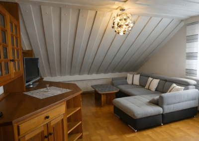 Gemütliches Wohnzimmer unter der Dachschräge mit Ecksofa, Couchtisch, Schrankwand und Fenster in der Ferienwohnung Jaeger in Viereth bei Bamberg.