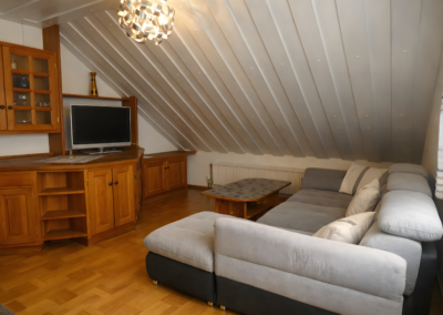 Wohnzimmer unter der Dachschräge mit großem Ecksofa, Couchtisch, Schrankwand und TV in der Ferienwohnung Jaeger in Viereth bei Bamberg.